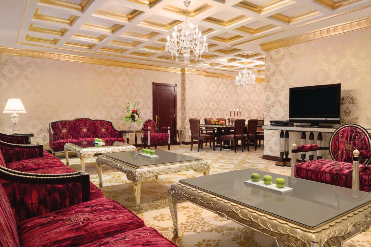 Grand Regency Doha, Trademark Collection By Wyndham Exterior photo The photo depicts an elegantly designed living room. The room features luxurious red sofas with ornate designs and metallic gold accents, arranged around glass-topped coffee tables that have intricate bases. A large, modern flat-screen television is 