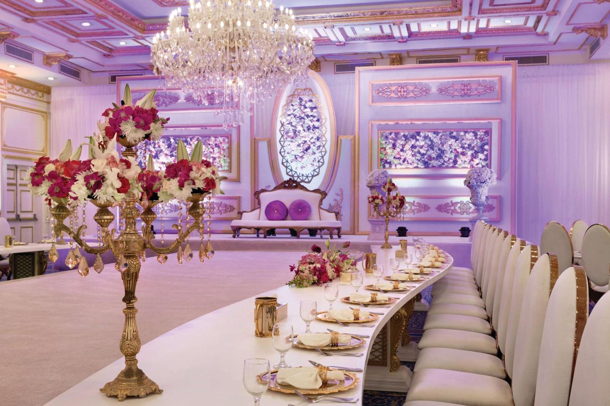 Grand Regency Doha, Trademark Collection By Wyndham Exterior photo The photo displays an elegantly decorated banquet or dining hall. It features a long, curved table set for a formal event, with fine china and floral centerpieces. Luxurious decorations include a grand chandelier hanging from the ceiling, and the wal