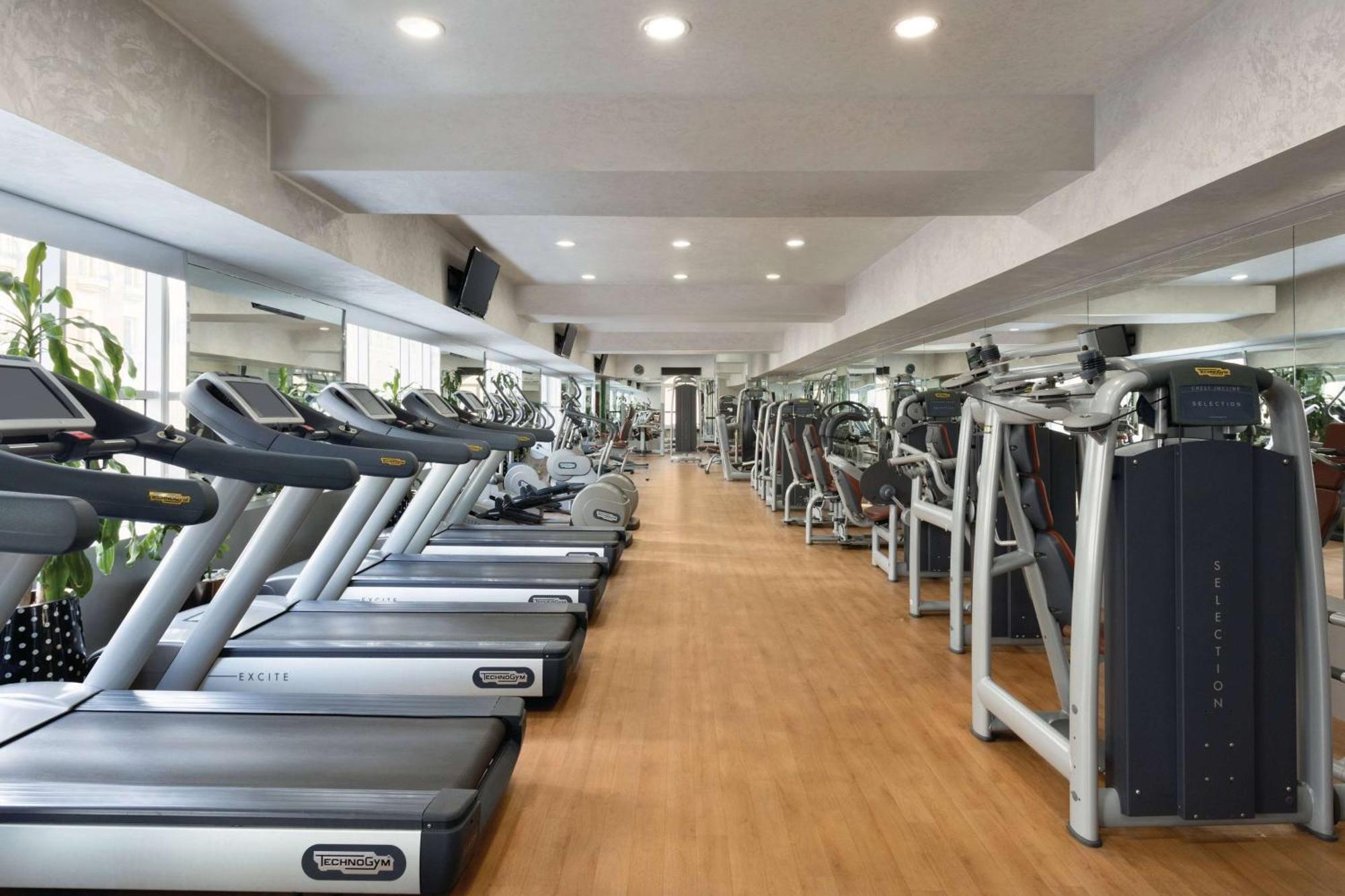 Grand Regency Doha, Trademark Collection By Wyndham Exterior photo The photo shows the interior of a gym or fitness center. It features a row of modern treadmills lined up against a wall, with a polished wooden floor. The space is brightly lit with recessed ceiling lights, and there are large mirrors on the walls, e