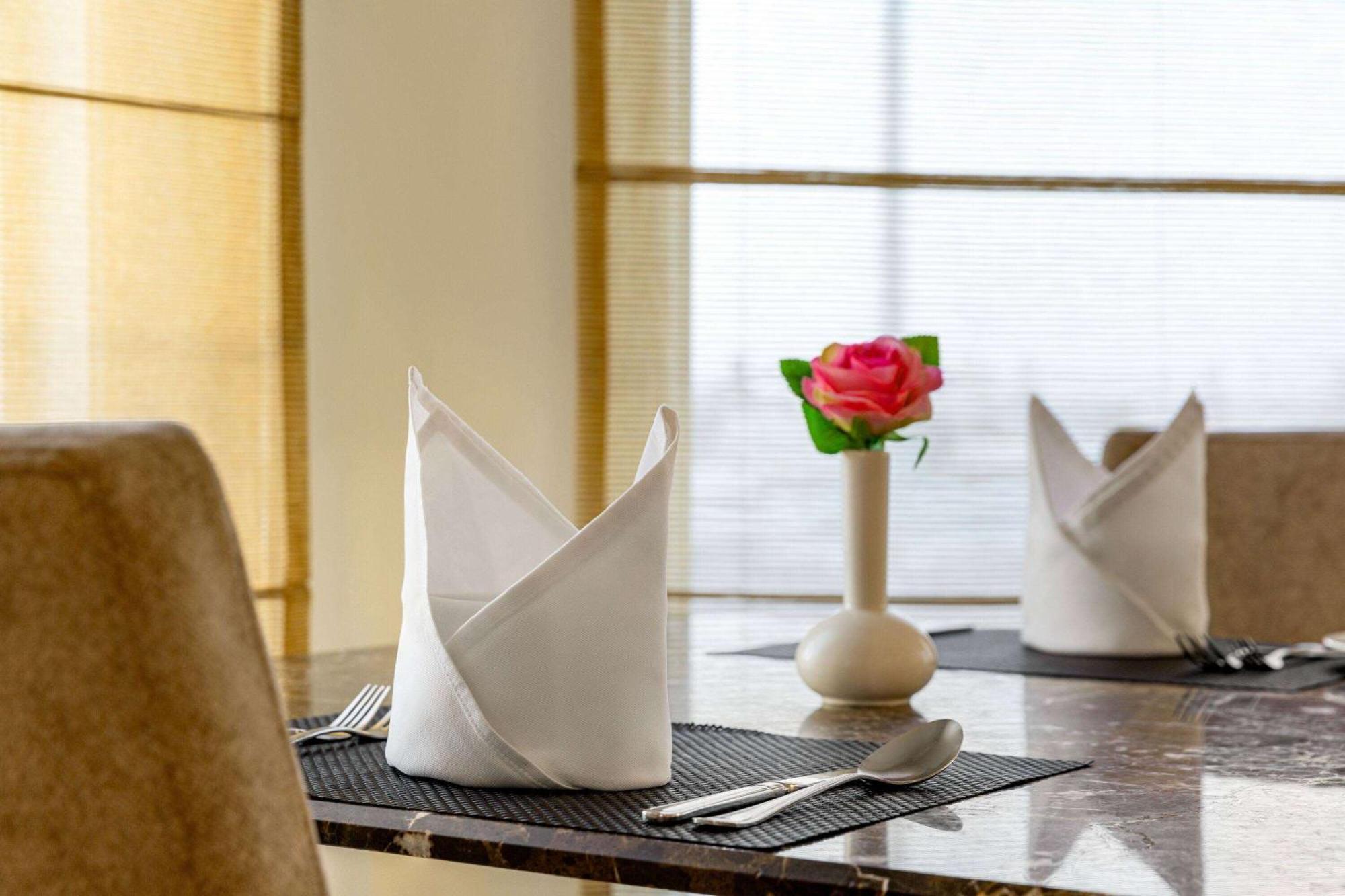 Grand Regency Doha, Trademark Collection By Wyndham Exterior photo The photo shows a neatly arranged dining table. On the table, there are two cloth napkins folded in a decorative way, one at each place setting. Silverware, including a knife and fork, is placed next to each napkin. In the center of the table, there 